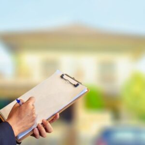 House in background & out of focus. Foreground of someone writing on a clipboard with warranty paper attached.